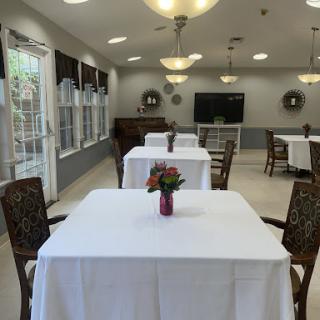 A well-lit dining area featuring neatly set tables with floral centerpieces, suitable for gatherings.