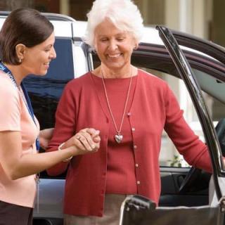 A caregiver assisting an elderly woman getting out of a car.