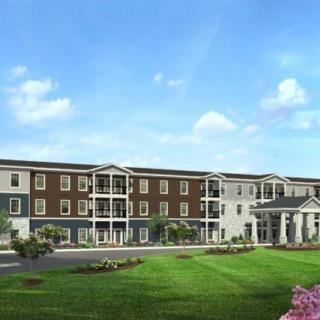 A modern residential apartment complex with a well-maintained lawn and clear blue sky.