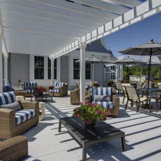 A sunny patio with comfortable wicker furniture under a pergola and an umbrella.