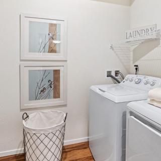 A clean and organized laundry room featuring a modern washer and dryer, with wall art and a laundry basket.