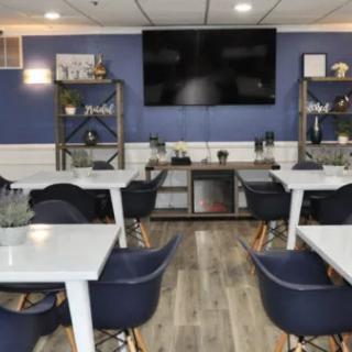 A modern cafe interior with tables, chairs, and a large television on the wall.