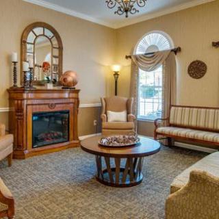 A cozy living room with a traditional design featuring a fireplace, armchair, and sofa arranged around a central coffee table.