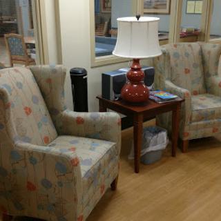 A cozy seating area featuring two patterned chairs, a small wooden table, and a lamp.