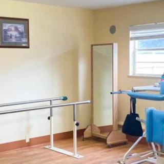 A physical therapy room equipped with parallel bars, a mirror, and a therapy chair.