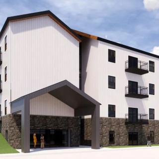 A modern multi-story building with a mix of stone and white exterior, featuring balconies and an entrance canopy.