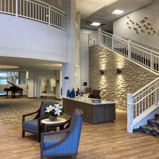 A modern lobby featuring a reception desk, comfortable seating, a grand staircase, and a piano.