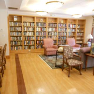A cozy library with bookshelves, armchairs, and a wooden floor.