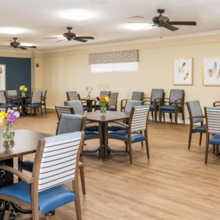 A bright and spacious dining room with neatly arranged tables and chairs, featuring decorative flowers on each table.