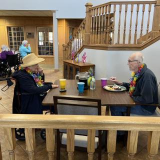 Two seniors enjoying a meal and conversation indoors.
