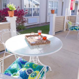 A cozy outdoor patio with a glass table, colorful cushions, and potted plants.