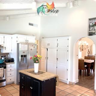 A bright, open kitchen with white cabinets and a central island, featuring stainless steel appliances and a view into the dining area.