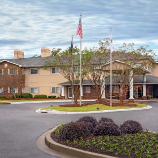 A view of a building with an entrance and flags, surrounded by landscaped greenery under a cloudy sky.