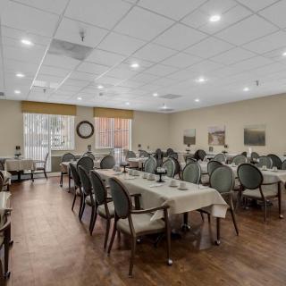 A spacious dining room with neatly arranged tables and chairs, featuring a warm wooden floor and soft lighting.