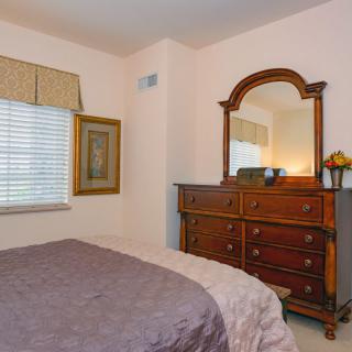A cozy bedroom featuring a dresser with a mirror, a neatly made bed, and a window with curtains.