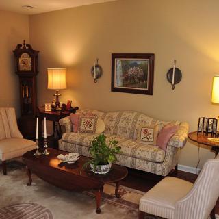 A cozy living room featuring traditional decor with a sofa, chairs, and a coffee table, accented by lamps and wall art.