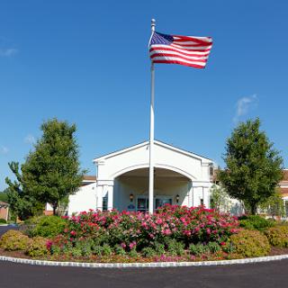 A picturesque view of a building with an American flag prominently displayed in front, surrounded by colorful flowers and greenery.