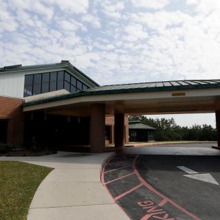 An entrance to a modern building with a covered driveway under a partly cloudy sky.