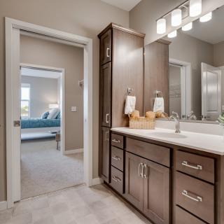 A modern bathroom with a sleek vanity, large mirror, and bright lighting leads into a bedroom.