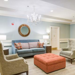 A cozy living room with a sofa, armchairs, and a large ottoman under a chandelier.