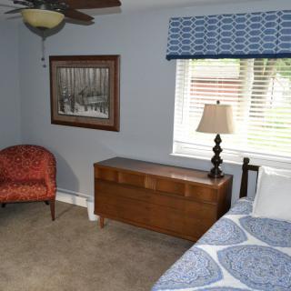 A cozy bedroom with a red chair, wooden chest, and bed beside a window.