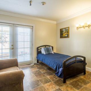 A cozy bedroom featuring a single bed with blue bedding, a comfortable chair, and ample natural light from large windows.