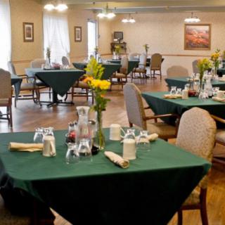 A neatly set dining area with green tablecloths and flower centerpieces.