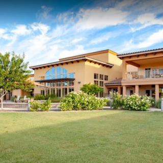 A large, modern building with a well-maintained lawn and landscaping under a partly cloudy sky.