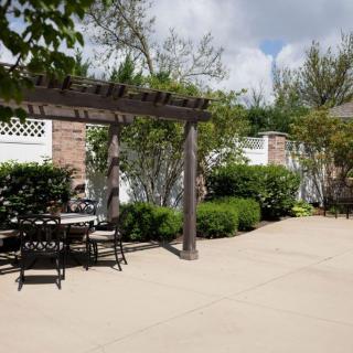 A sunny patio garden with a pergola and outdoor seating surrounded by lush greenery.