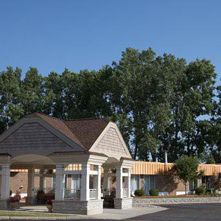 A building entrance with a canopy surrounded by trees under a clear blue sky.