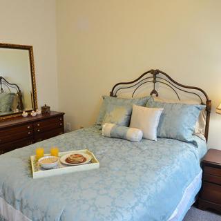 A cozy bedroom with a neatly made bed, decorative pillows, and a breakfast tray. A mirror is placed above a dresser next to the bed.
