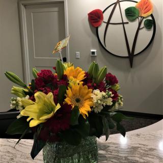A vibrant bouquet of flowers arranged in an office setting, with a decorative wall piece in the background.