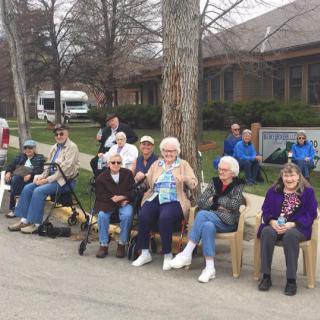 A group of people sitting on chairs and benches outdoors, enjoying a community gathering.