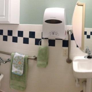 A bathroom featuring a sink, mirror, hand dryer, and towels against a tiled wall.