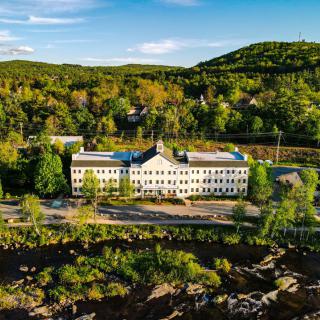 An aerial view of a large building surrounded by lush trees and rolling hills under a clear blue sky.