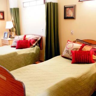 A cozy bedroom featuring twin beds with colorful pillows and green curtains.