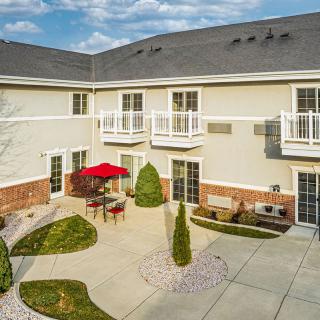 A well-maintained courtyard with outdoor seating and a red umbrella, surrounded by a two-story building.