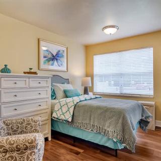 A cozy bedroom with a bed, dresser, and a large window providing natural light.