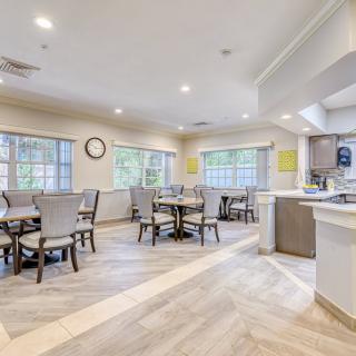 A modern dining area with multiple tables and chairs, featuring large windows and a clean, bright interior.