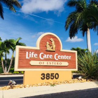 A sign for Life Care Center of Estero with palm trees and a clear sky in the background.