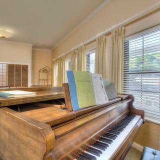 A cozy music room featuring a piano with sheet music on the stand, bathed in natural light from large windows.