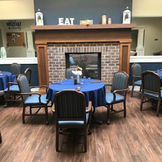 A cozy dining area with blue tablecloths, a central fireplace, and inviting decor.