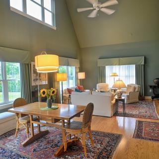 A spacious living room with a dining area, showcasing modern decor, wood flooring, and large windows offering ample natural light.