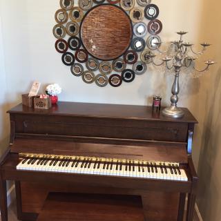 A cozy corner featuring a piano with a decorative mirror and candlestick.