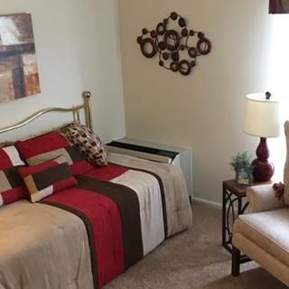 A cozy bedroom with modern decor, featuring a neatly made bed, wall art, and a lamp on a side table.