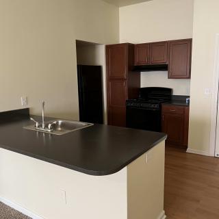 A modern apartment kitchen featuring dark countertops and wooden cabinetry.