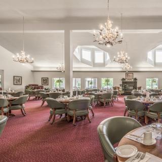 An elegant dining room featuring chandeliers, neatly arranged tables, and green upholstered chairs.