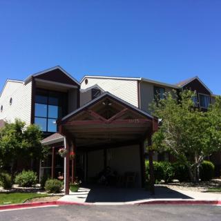 A sunny day view of a building entrance surrounded by greenery under a clear blue sky.