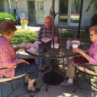 A group of three people enjoying a meal together at an outdoor table in a garden setting.