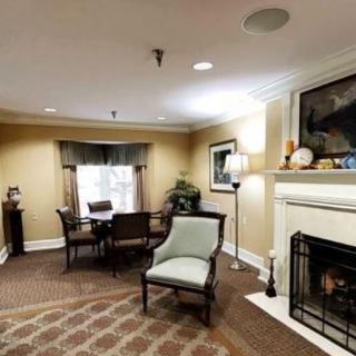 A cozy living room with a fireplace, chairs, and a table near a window.